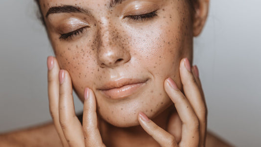A close-up of a woman with glowy skin holding her face wit her eyes closed.