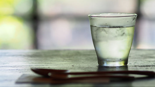 A glass of water and a spoon lying on a wooden table.
