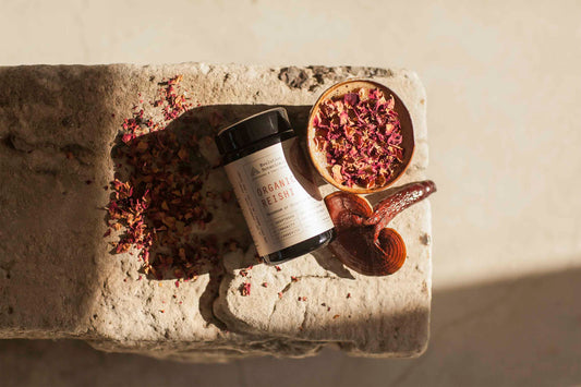 Evolution Botanicals jar of Reishi lying horizontally on a stone next to a Reishi mushroom and rose petals in a bowl.
