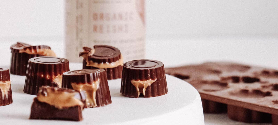 Chocolates sitting on a pedestal with their inner liquids oozing out from them with a out of focus jar of Organic Reishi in the background.