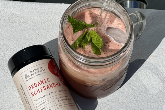 A jar of Evolution Botanicals Schisandra lying horizontally next to a mason jar with a handle containing a drink made with Schisandra