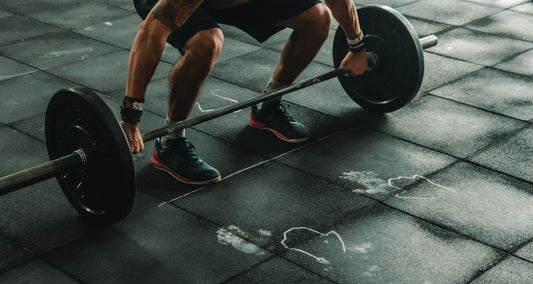 A shot of a man bending down to lift a bar with weights on it.