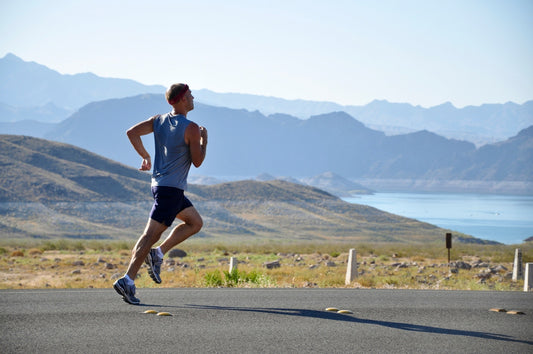 A man running on a road with a hilly landscape in the background.
