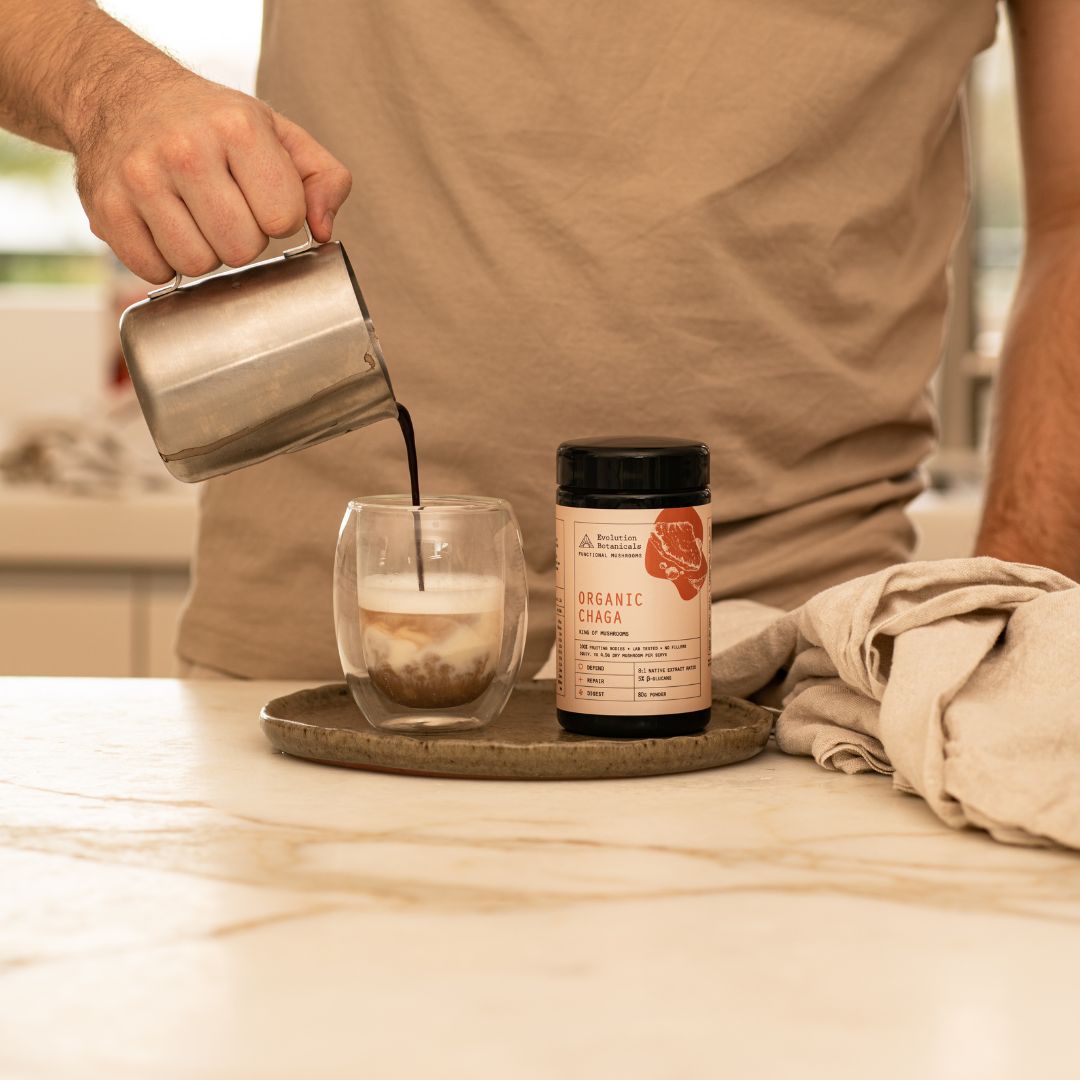 A close-up of a 100g jar of Organic Chaga next to a glass cup with liquid being poured into it from a metal pourer