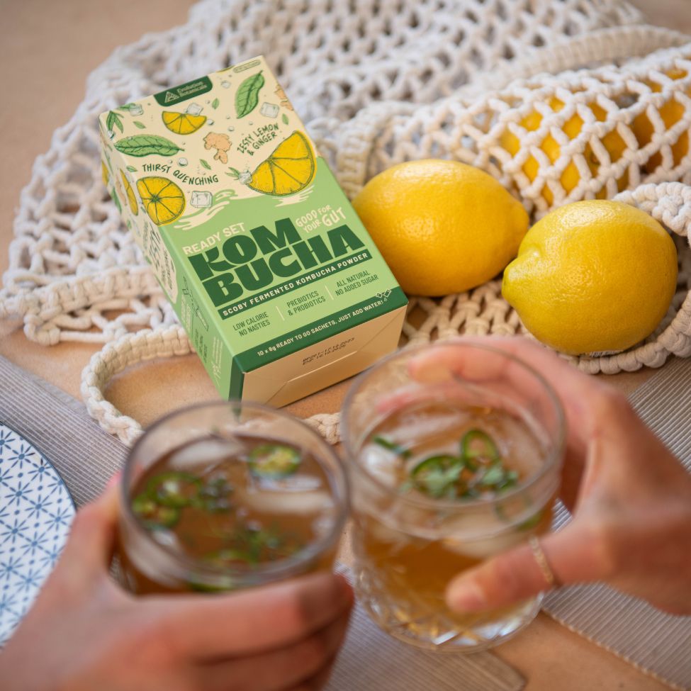 Two people clinking glasses of kombucha in front of a box of Ready Set Kombucha