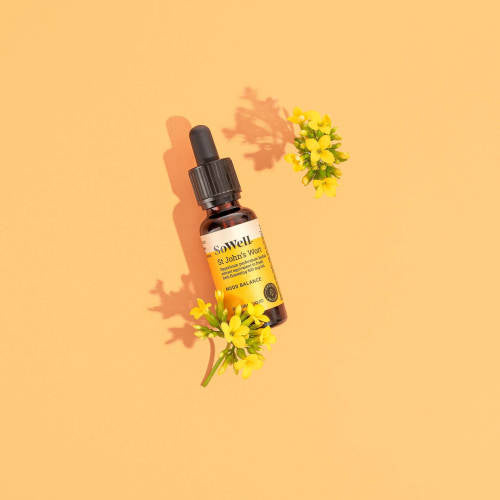 A wide shot of a 30ml dropper bottle of Sowell St John's Wort tincture on a yellowish background surrounded by flowers