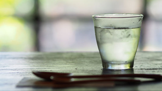 A glass of water and a spoon lying on a wooden table. 