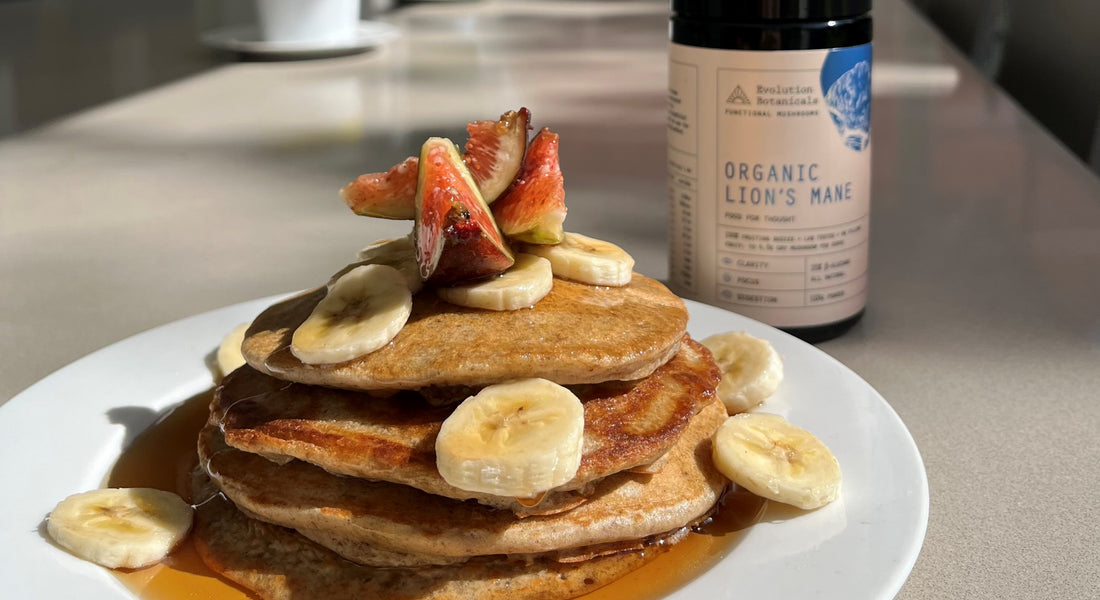 Lion's Mane pancakes on a plate with bananas and strawberries sitting on top of it with a jar of Evolution Botanicals' Lion's Mane sitting behind it. 