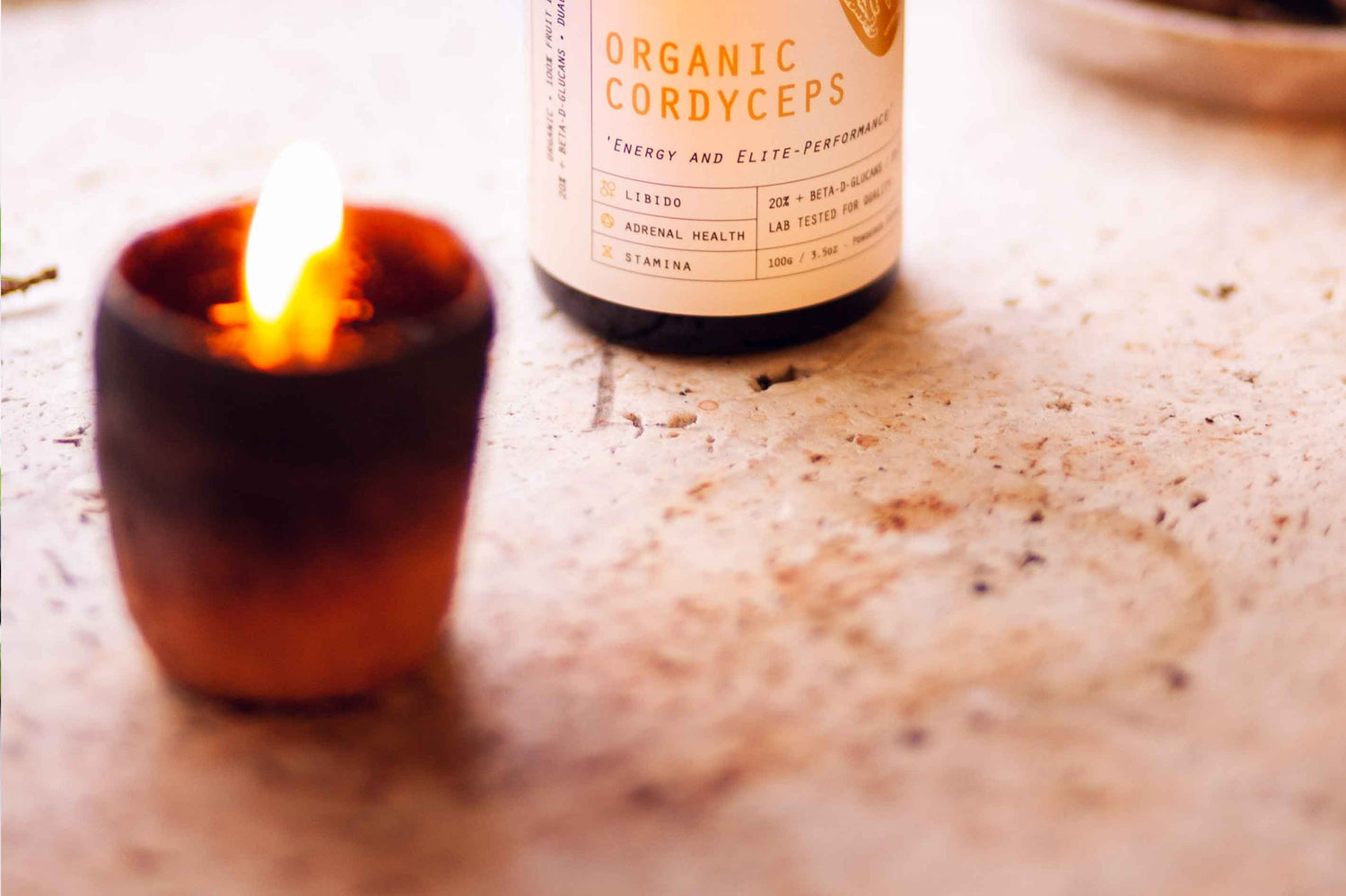 A lit candle on a table next to a jar of Evolution Botanicals Organic Cordyceps