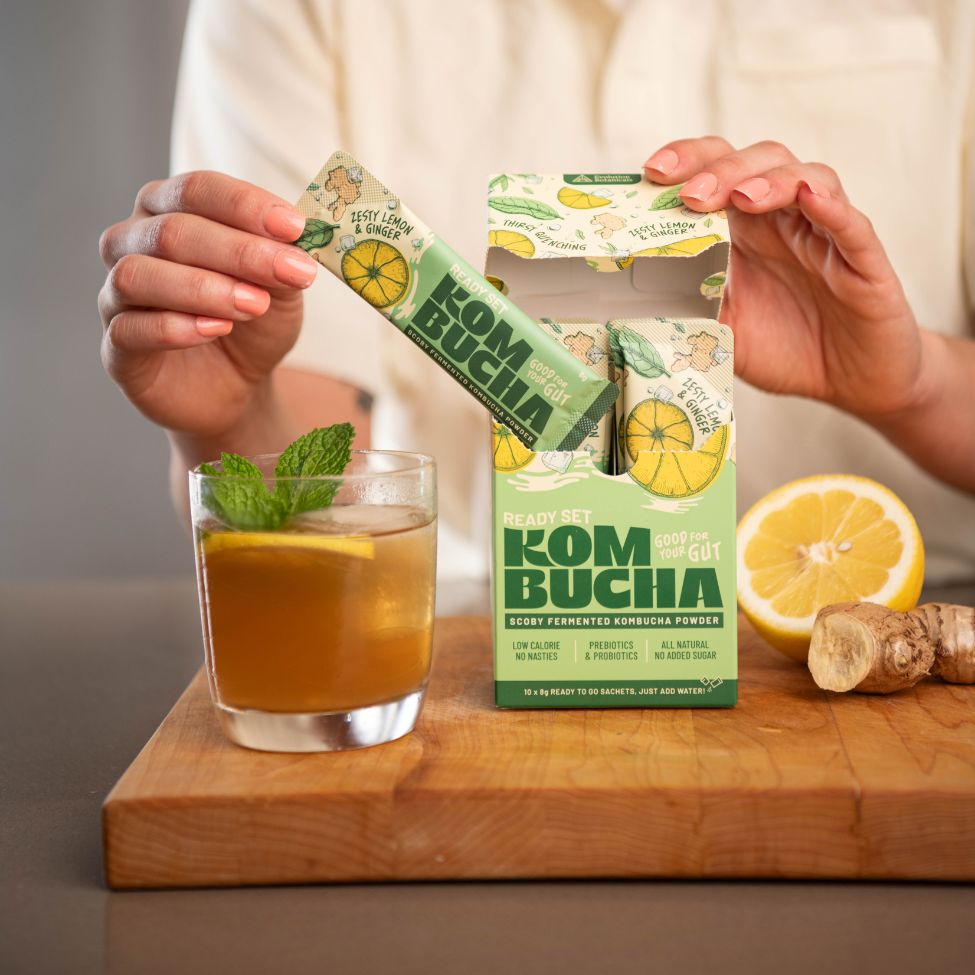 A person pulling a sachet of Kombucha out of the cardboard box next to a prepared drink