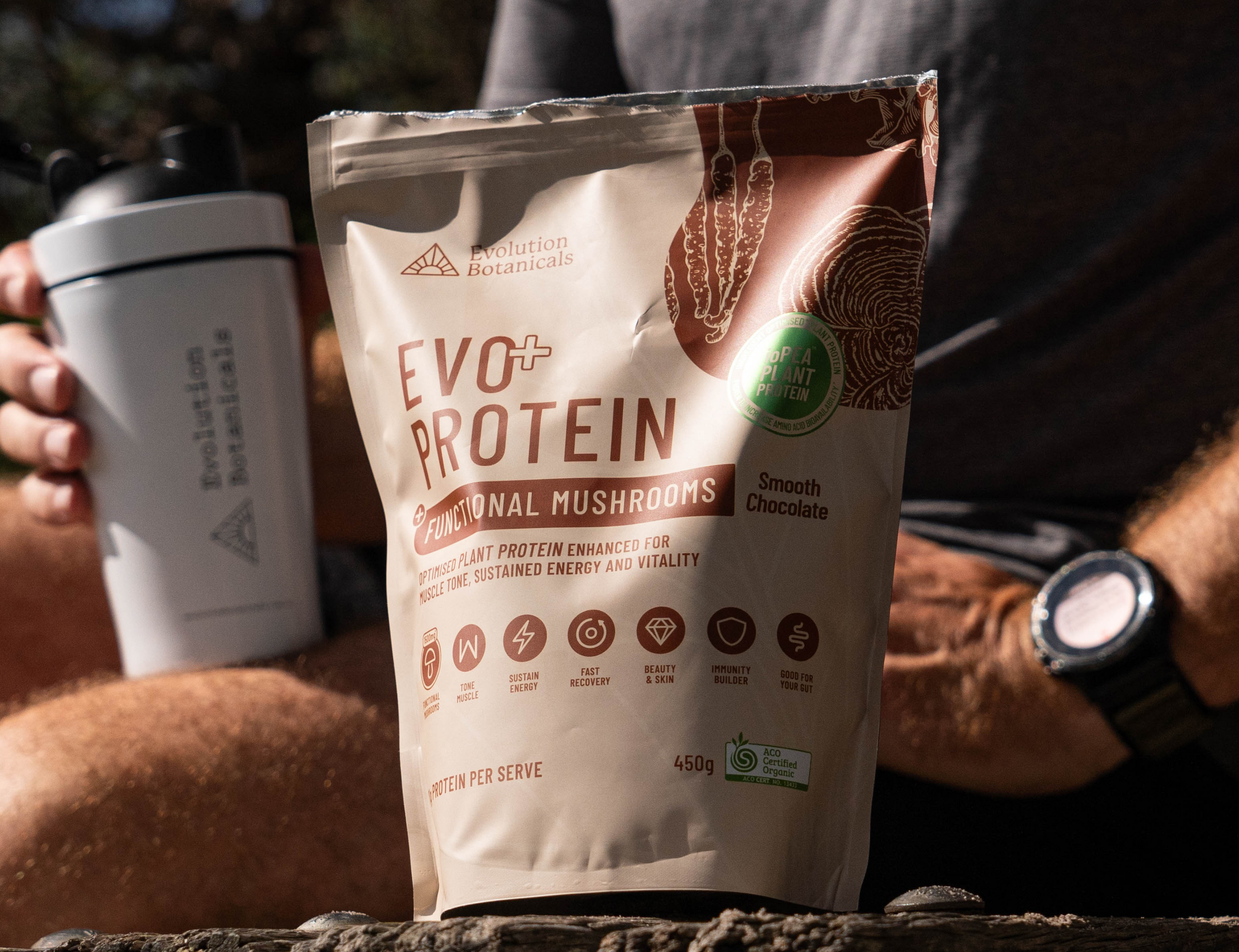Evo+ Smooth Chocolate bag sitting on a rock ledge, with a person sitting behind with a shaker bottle. 