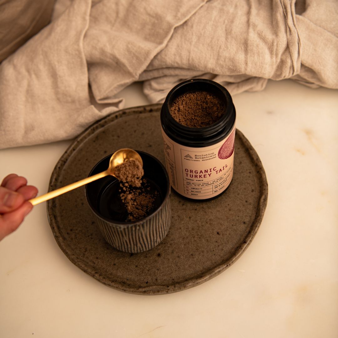 A person spooning brown powder into a ceramic mug next to a 100g jar of Organic Turkey Tail