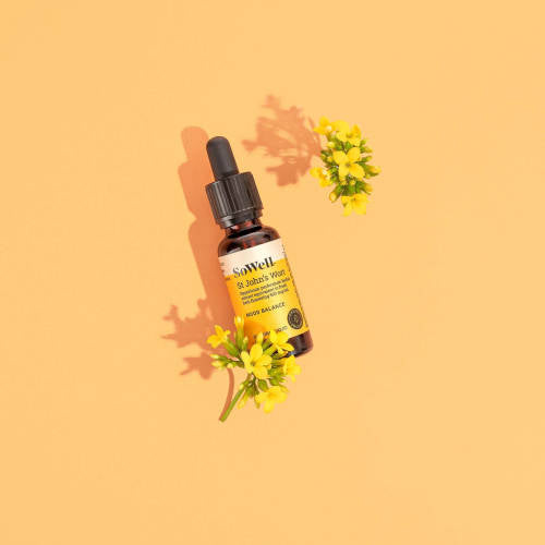 A wide shot of a  30ml dropper bottle of Sowell St John's Wort tincture on a yellowish background surrounded by flowers